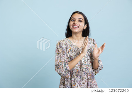 Confident pleased woman applauding in front of the camera and cheering for success, standing ovation for personal achievement. Indian girl ecstatic in admiration clapping hands in studio. 125072260