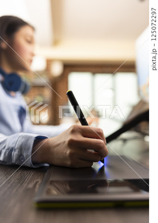 Closeup of asian designer using stylus on digital drawing pad to fine tune and edit photos. Selective focus on individual adjusting color balance with graphic tablet, enhancing images for magazine use 125072297
