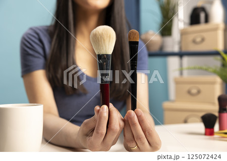 Closeup of social media influencer presenting two makeup brushes, holding them close to camera for a detailed view. Beauty vlogger making content about cosmetic equipment for face painting. Closeup of social media influencer presenting two makeup brushes, holding them close to camera for a detailed view. Beauty vlogger making content about cosmetic equipment for face painting. 125072424