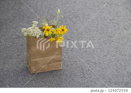 white and yellow wild flowers in a paper bag on the background of an asphalt road 125072559