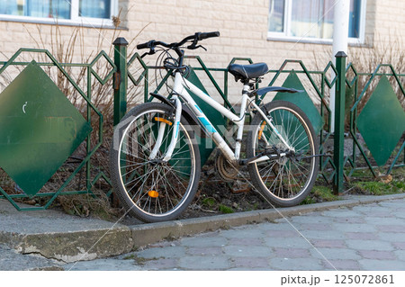 White and blue bicycle leaning against green metal fence in urban setting White and blue bicycle leaning against green metal fence in urban setting 125072861