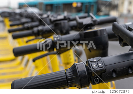 Row of yellow electric scooters ready for rent showing control panel and grips 125072873
