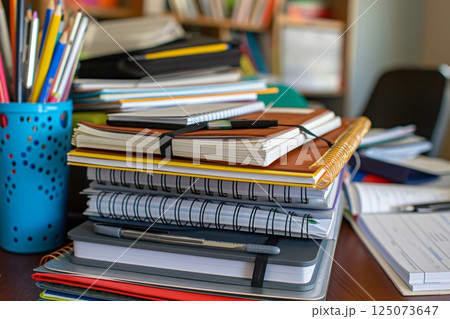 Stack of notebooks and books is sitting on a desk, representing the concept of studying and learning 125073647