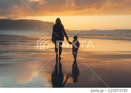 Mother and her son are enjoying a peaceful walk on the beach as the sun sets, casting long shadows on the wet sand Mother and her son are enjoying a peaceful walk on the beach as the sun sets, casting long shadows on the wet sand 125073785