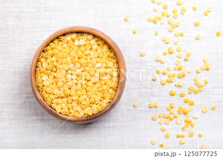 Yellow lentils in a wooden bowl on linen. Dried seeds of a Lens esculenta variety, a legume of small, round, and yellow fruits. High in protein and fiber, with soft and creamy texture, when cooked. 125077725
