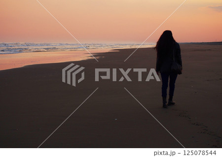 夕暮れの浜辺を歩く女性 125078544
