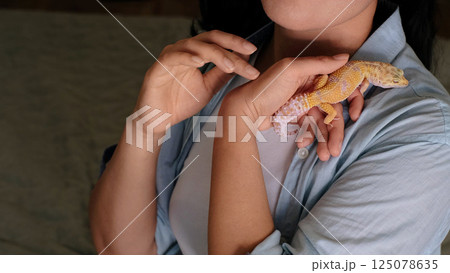 A leopard gecko rests securely in a woman s hands as she cradles it near her chest. This scene reflects the growing appreciation for reptiles as calming and unique companions. 125078635