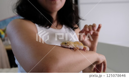 A woman gently pets a leopard gecko resting on her arm, highlighting its vivid colors. This image showcases human compassion for exotic animals and the growing trend of ethical pet ownership. A woman gently pets a leopard gecko resting on her arm, highlighting its vivid colors. This image showcases human compassion for exotic animals and the growing trend of ethical pet ownership. 125078646