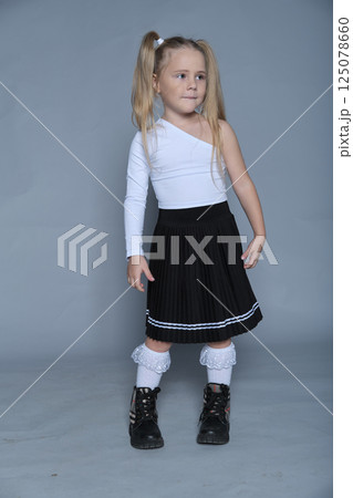 A 5-year-old girl poses confidently in a stylish one-shoulder top and pleated skirt during a studio shoot, showing her potential in children's fashion. 125078660