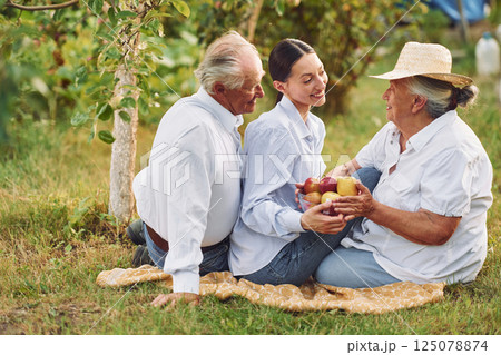 With apples. Sitting on the ground. Daughter is with her senior mother and father is in the garden 125078874