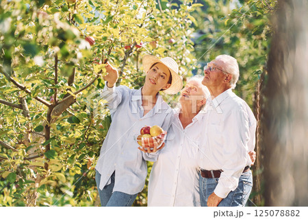 Holding fresh apples. Daughter is with her senior mother and father is in the garden 125078882