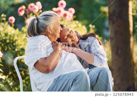 Sitting and embracing each other. Young woman is with her senior mother is in the garden Sitting and embracing each other. Young woman is with her senior mother is in the garden 125078943