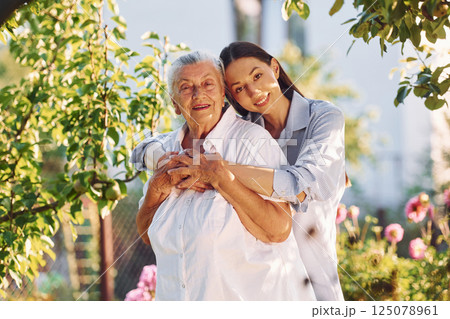 Embracing and posing for a camera. Young woman is with her senior mother is in the garden 125078961