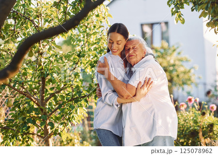 Embracing and posing for a camera. Young woman is with her senior mother is in the garden 125078962