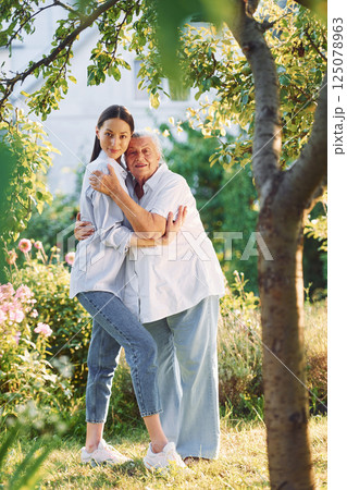 Embracing and posing for a camera. Young woman is with her senior mother is in the garden 125078963