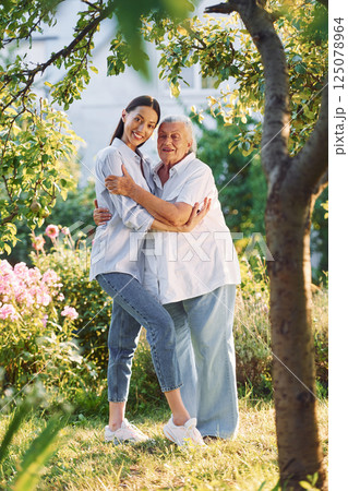 Embracing and posing for a camera. Young woman is with her senior mother is in the garden 125078964