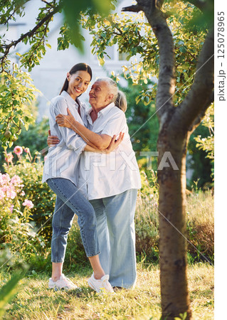 Embracing and posing for a camera. Young woman is with her senior mother is in the garden 125078965