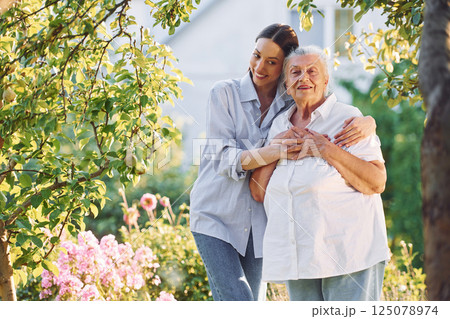 Embracing and smiling. Young woman is with her senior mother is in the garden Embracing and smiling. Young woman is with her senior mother is in the garden 125078974