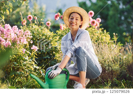 Preparing for watering the flowers. Young cheerful woman is in the garden at daytime 125079026