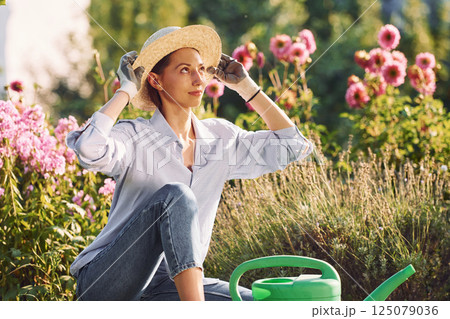 Sitting with watering can. Young cheerful woman is in the garden at daytime Sitting with watering can. Young cheerful woman is in the garden at daytime 125079036