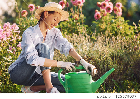 Sitting with watering can. Young cheerful woman is in the garden at daytime Sitting with watering can. Young cheerful woman is in the garden at daytime 125079037
