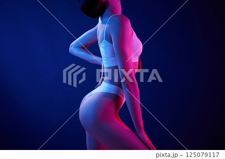 Side view. Young woman in underwear is in the studio with neon lights Side view. Young woman in underwear is in the studio with neon lights 125079117