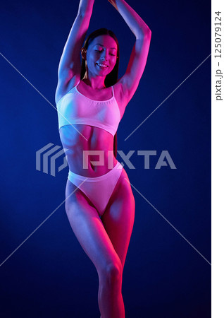Standing with hands up. Young woman in underwear is in the studio with neon lights 125079124