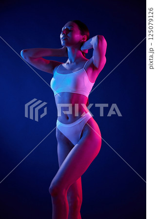 Showing body. Young woman in underwear is in the studio with neon lights Showing body. Young woman in underwear is in the studio with neon lights 125079126