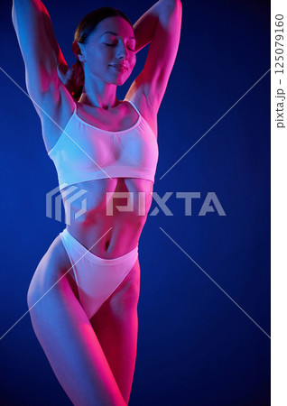 Slim body type. Young woman in underwear is in the studio with neon lights Slim body type. Young woman in underwear is in the studio with neon lights 125079160