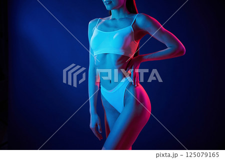 Taking a closer look. Young woman in underwear is in the studio with neon lights Taking a closer look. Young woman in underwear is in the studio with neon lights 125079165