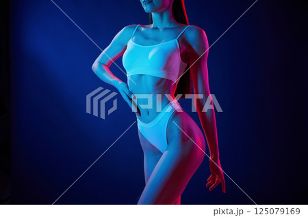 Taking a closer look. Young woman in underwear is in the studio with neon lights 125079169