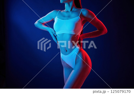 Taking a closer look. Young woman in underwear is in the studio with neon lights 125079170