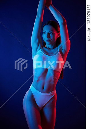 Model is standing and posing. Young woman in underwear is in the studio with neon lights Model is standing and posing. Young woman in underwear is in the studio with neon lights 125079175