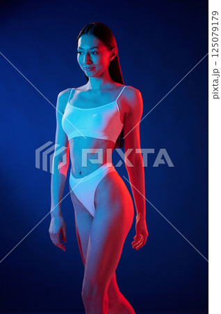 Beautiful slim body type. Young woman in underwear is in the studio with neon lights Beautiful slim body type. Young woman in underwear is in the studio with neon lights 125079179