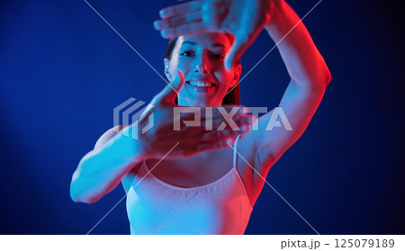 Doing gestures by the hands. Young woman in underwear is in the studio with neon lights Doing gestures by the hands. Young woman in underwear is in the studio with neon lights 125079189