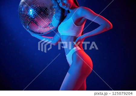 With shiny mirrored ball. Young woman in underwear is in the studio with neon lights 125079204