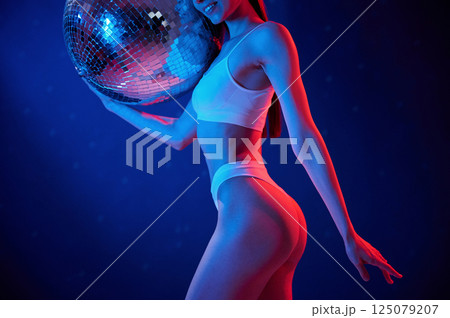 With shiny mirrored ball. Young woman in underwear is in the studio with neon lights With shiny mirrored ball. Young woman in underwear is in the studio with neon lights 125079207