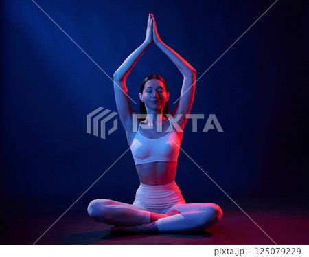 Lotus pose. Young woman in sportive clothes is in the studio with neon lights 125079229