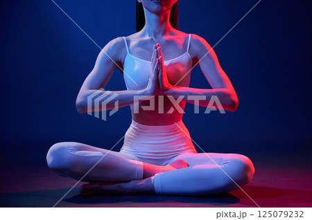 Lotus pose. Young woman in sportive clothes is in the studio with neon lights 125079232