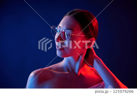 In eyewear. Portrait of young woman that is indoors in neon lighting In eyewear. Portrait of young woman that is indoors in neon lighting 125079266
