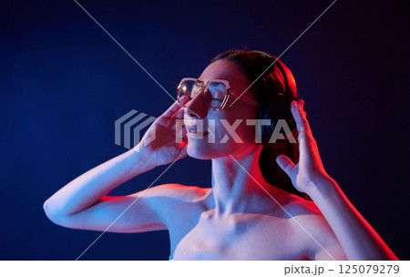 Enjoying music by using headphones. Portrait of young woman that is indoors in neon lighting Enjoying music by using headphones. Portrait of young woman that is indoors in neon lighting 125079279
