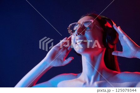 Feel the music. In headphones. Portrait of young woman that is indoors in neon lighting 125079344