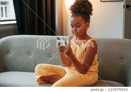 Surfing the internet by using smartphone. Cute black girl in casual clothes is at home at daytime 125079503