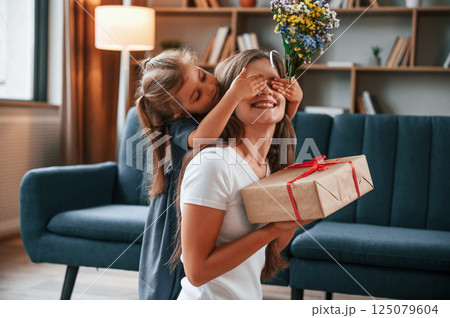 Girl is giving the box with a gift. Young mother with her daughter is together at apartment Girl is giving the box with a gift. Young mother with her daughter is together at apartment 125079604