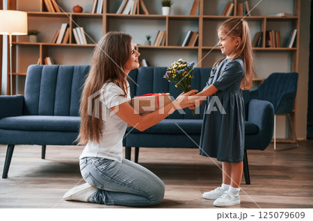 Girl is giving beautiful flowers to a woman. Young mother with her daughter is together at apartment Girl is giving beautiful flowers to a woman. Young mother with her daughter is together at apartment 125079609