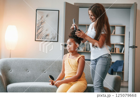 Mother is combs hair. Young woman with her daughter is together at apartment 125079668