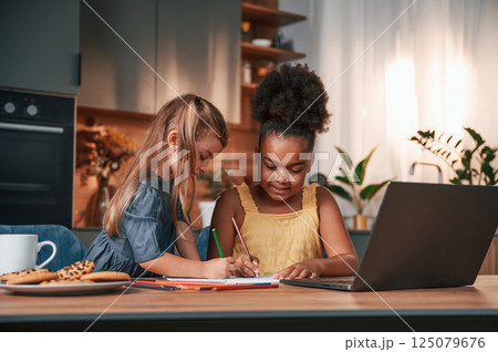 Two little girls sitting by the table and drawing Two little girls sitting by the table and drawing 125079676
