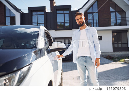 In white clothes. Young stylish man is with electric car at daytime 125079898