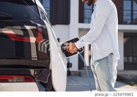 Process of charging the vehicle. Young stylish man is with electric car at daytime 125079901