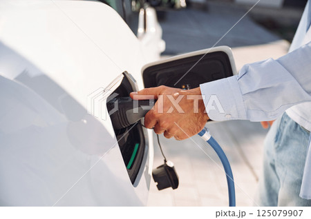 Plugged in charger. Close up view of man with his electric car 125079907